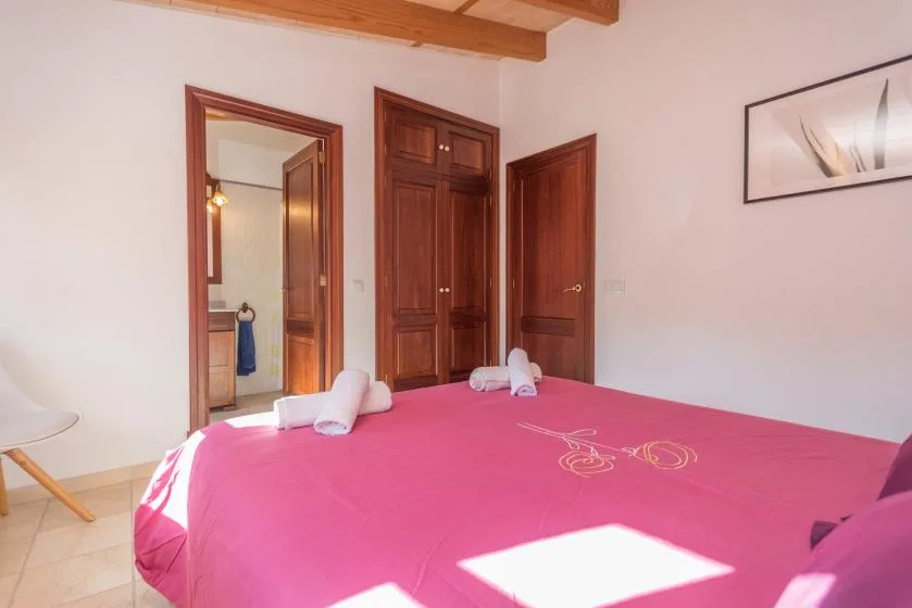 A bedroom with a bed covered in pink bedding and wooden doors.