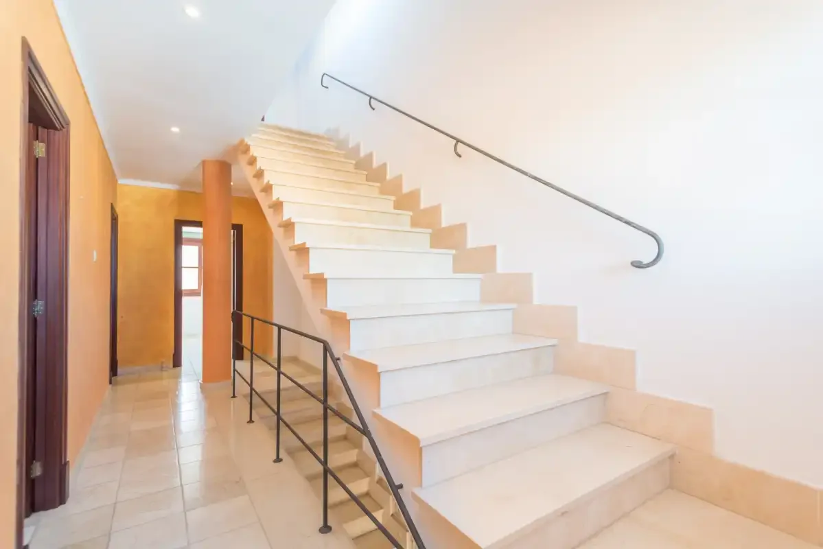 A bright interior hallway with a staircase and dark metal railing.