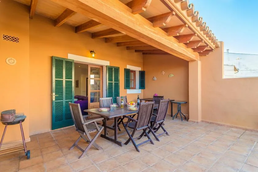 Comedor exterior cubierto con una mesa y asientos junto a unas puertas abiertas.