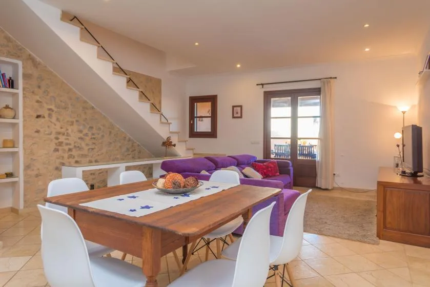 Sala de estar y comedor con una mesa de madera y asientos morados.