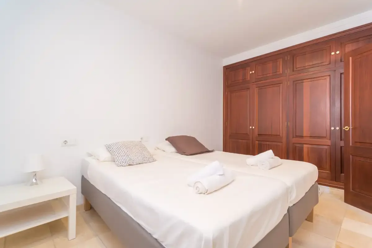 A bright bedroom with a double bed and built-in wooden wardrobes.