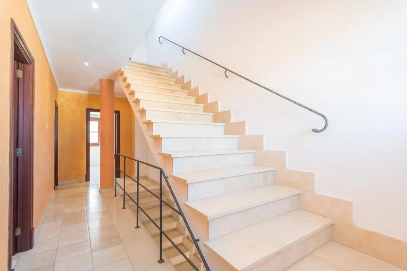 A tiled interior hallway with a staircase and a wall-mounted handrail.