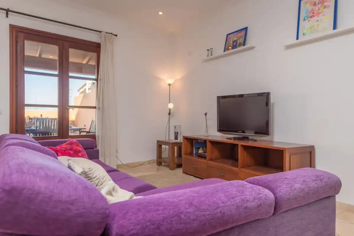 A living room with purple seating, a television, and a wooden media console.