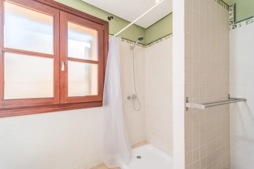 A tiled bathroom with a shower beside a wooden-framed window.
