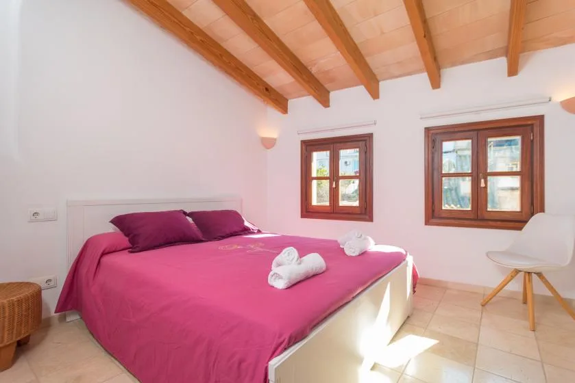 A bedroom with a pink bed and two wooden-framed windows.