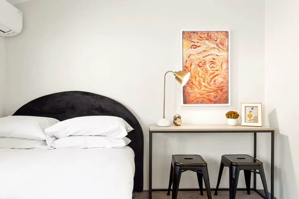 Un dormitorio con una cama, un escritorio y una obra colorida enmarcada.