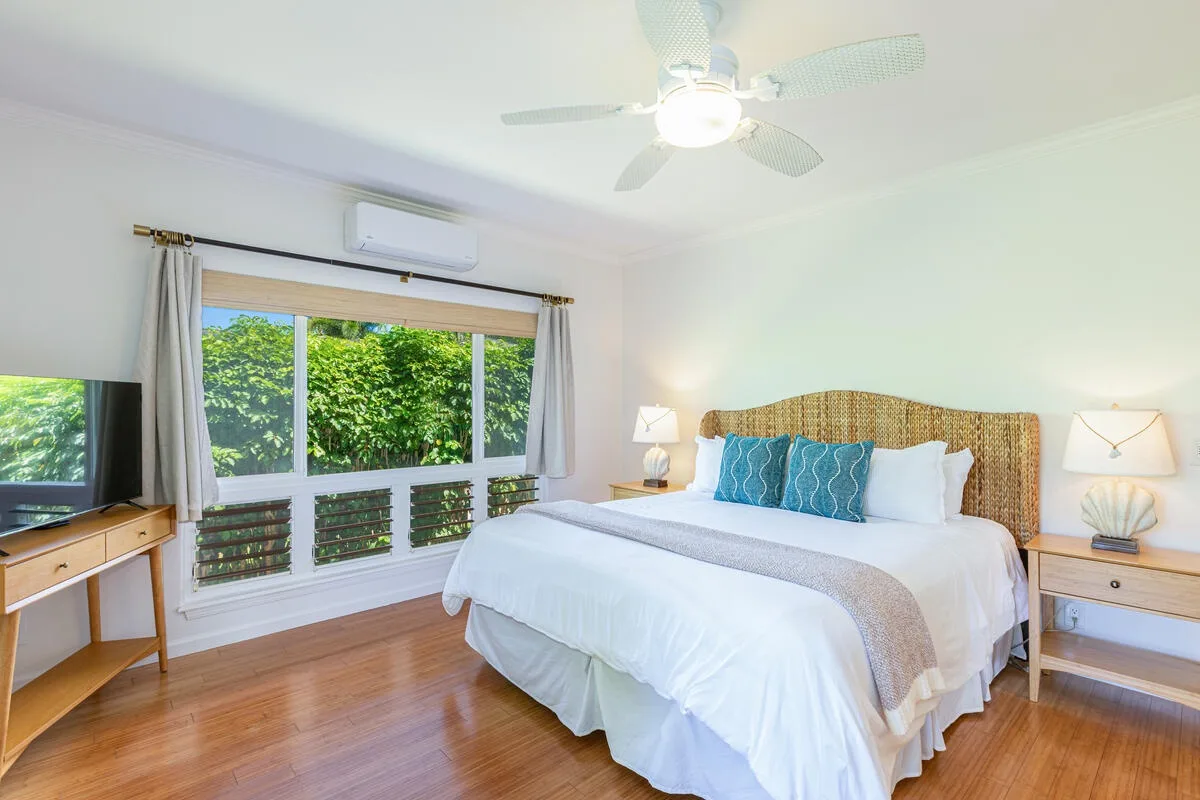 Un dormitorio luminoso con una cama, mesitas de noche y una ventana grande con vistas a la vegetación.
