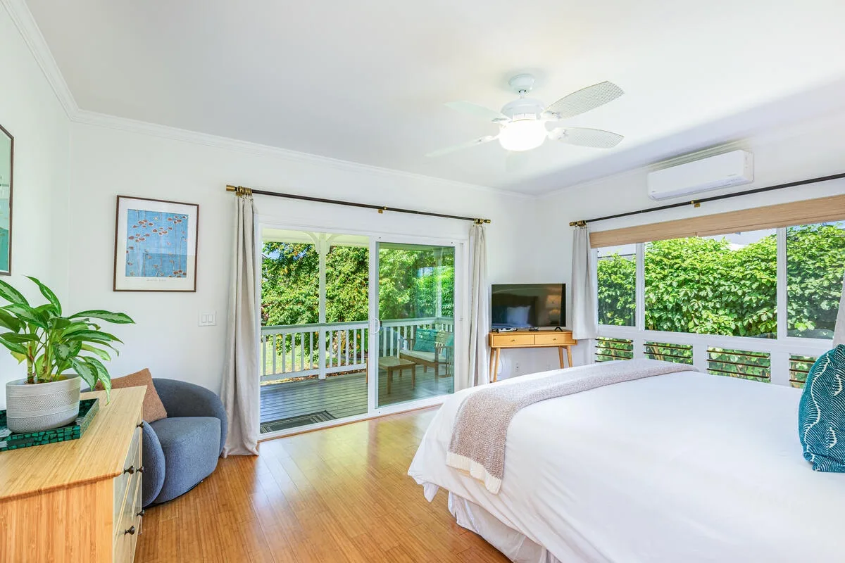 Un dormitorio luminoso con una cama grande, un televisor y ventanas con vistas a la vegetación.