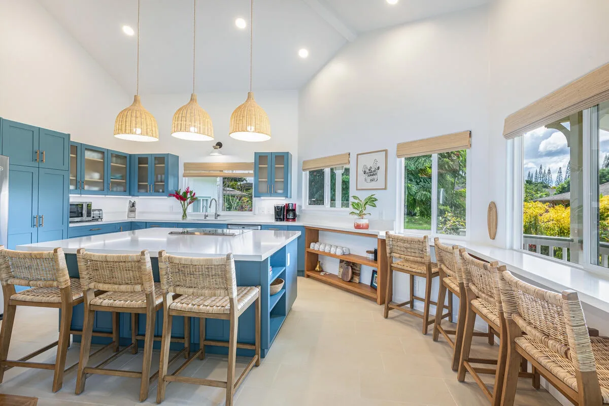 Una cocina luminosa con una isla central, asientos tejidos y grandes ventanas.