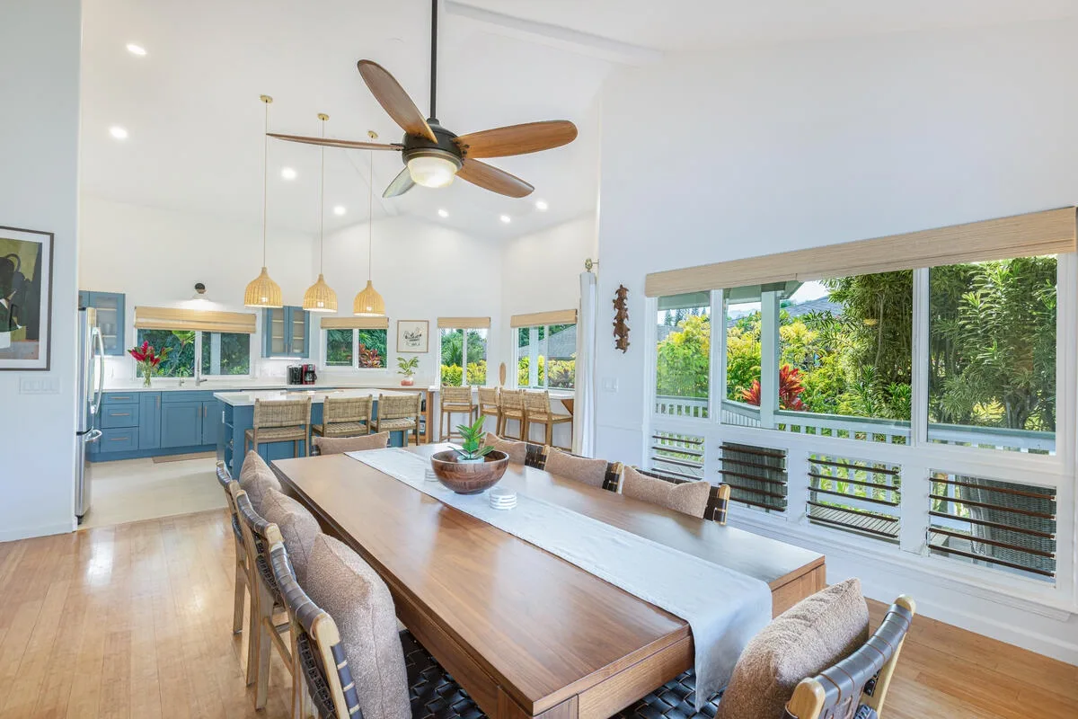 Un comedor luminoso con una mesa larga junto a una cocina y grandes ventanas.