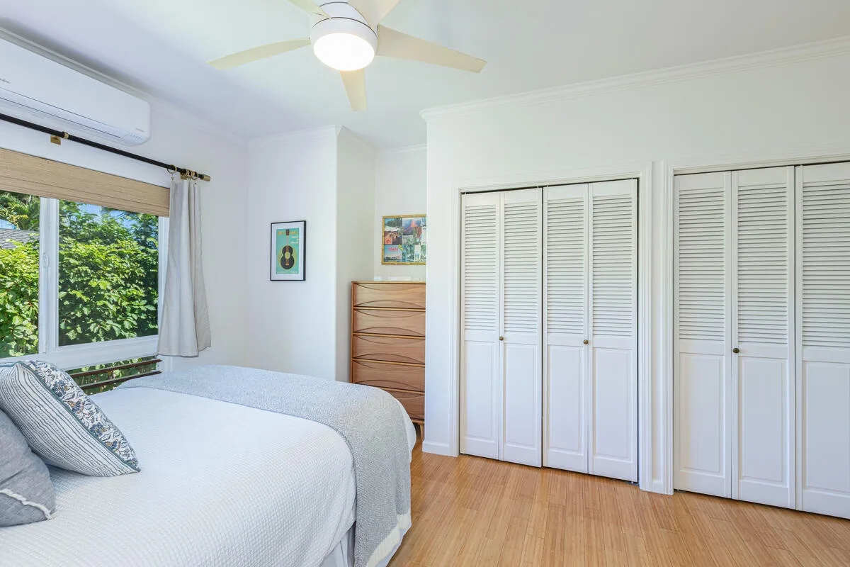Un dormitorio luminoso con una cama, suelo de madera y puertas blancas de armario con persianas.
