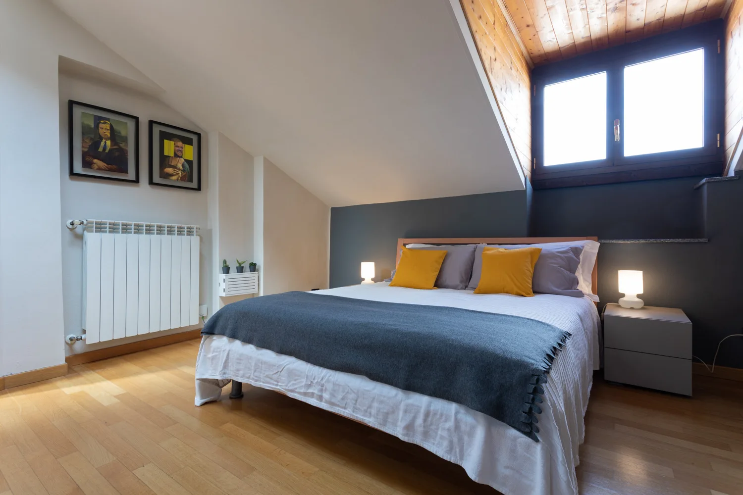 Un dormitorio con una cama grande bajo un techo inclinado y una ventana luminosa.