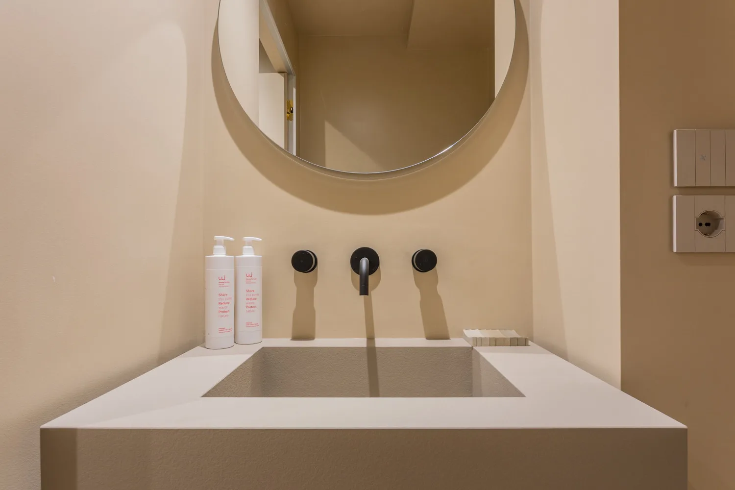 A bathroom vanity with a basin, wall-mounted fixtures, and a round mirror.