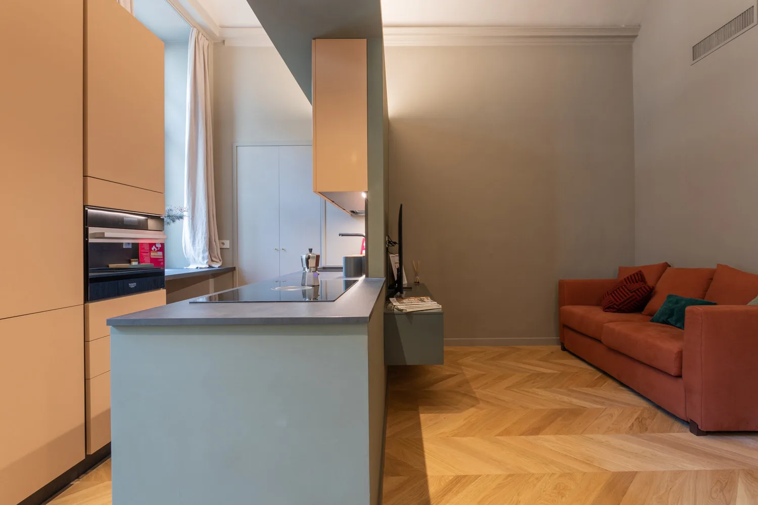 A modern kitchen opens onto a living area with orange seating.