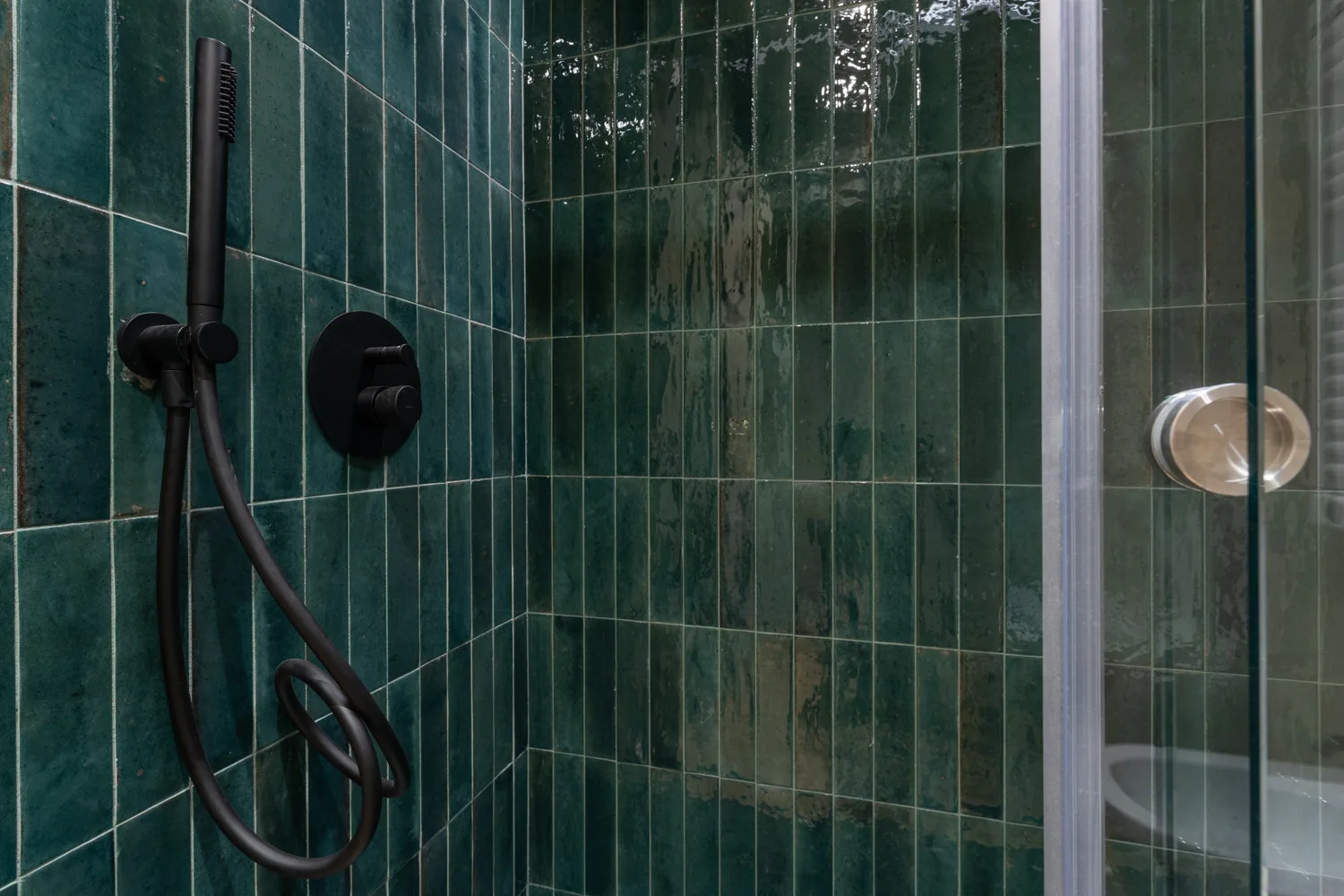 A tiled shower with a handheld showerhead and glass panels.