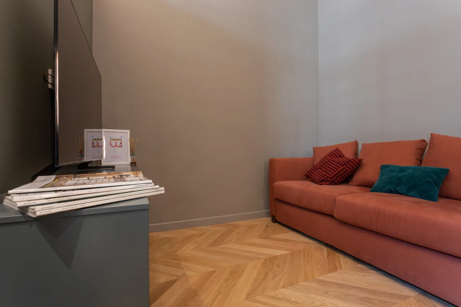 A living room with a television, a coral-colored sofa, and a wood floor.