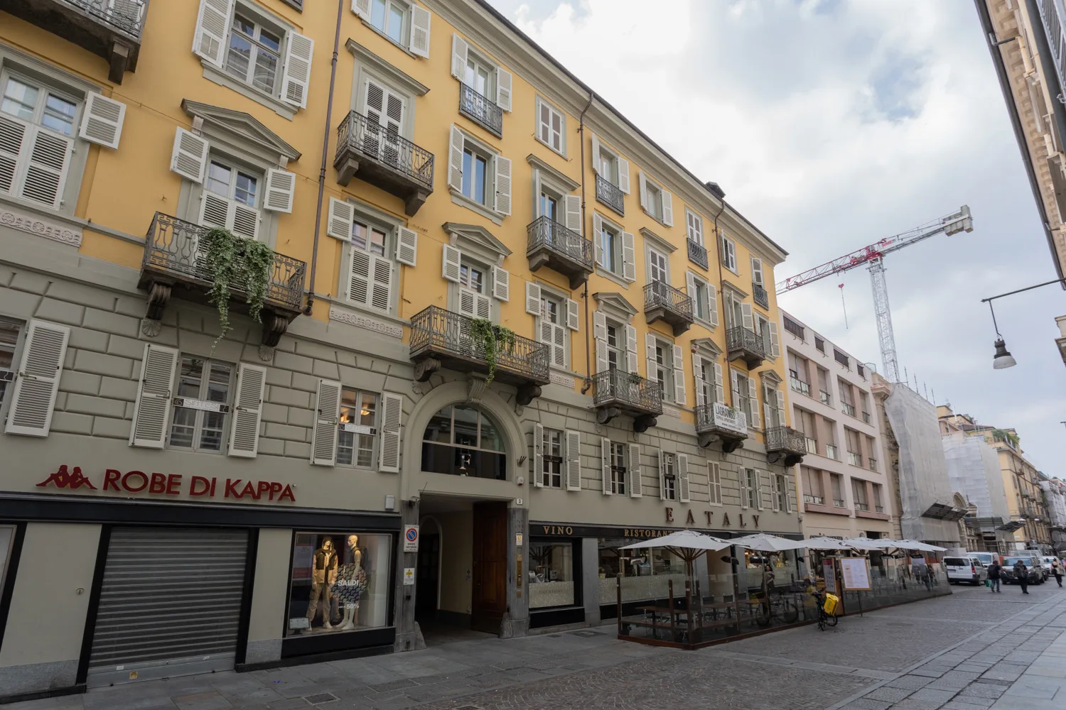 A street view of a yellow multi-story building with shops and outdoor seating.