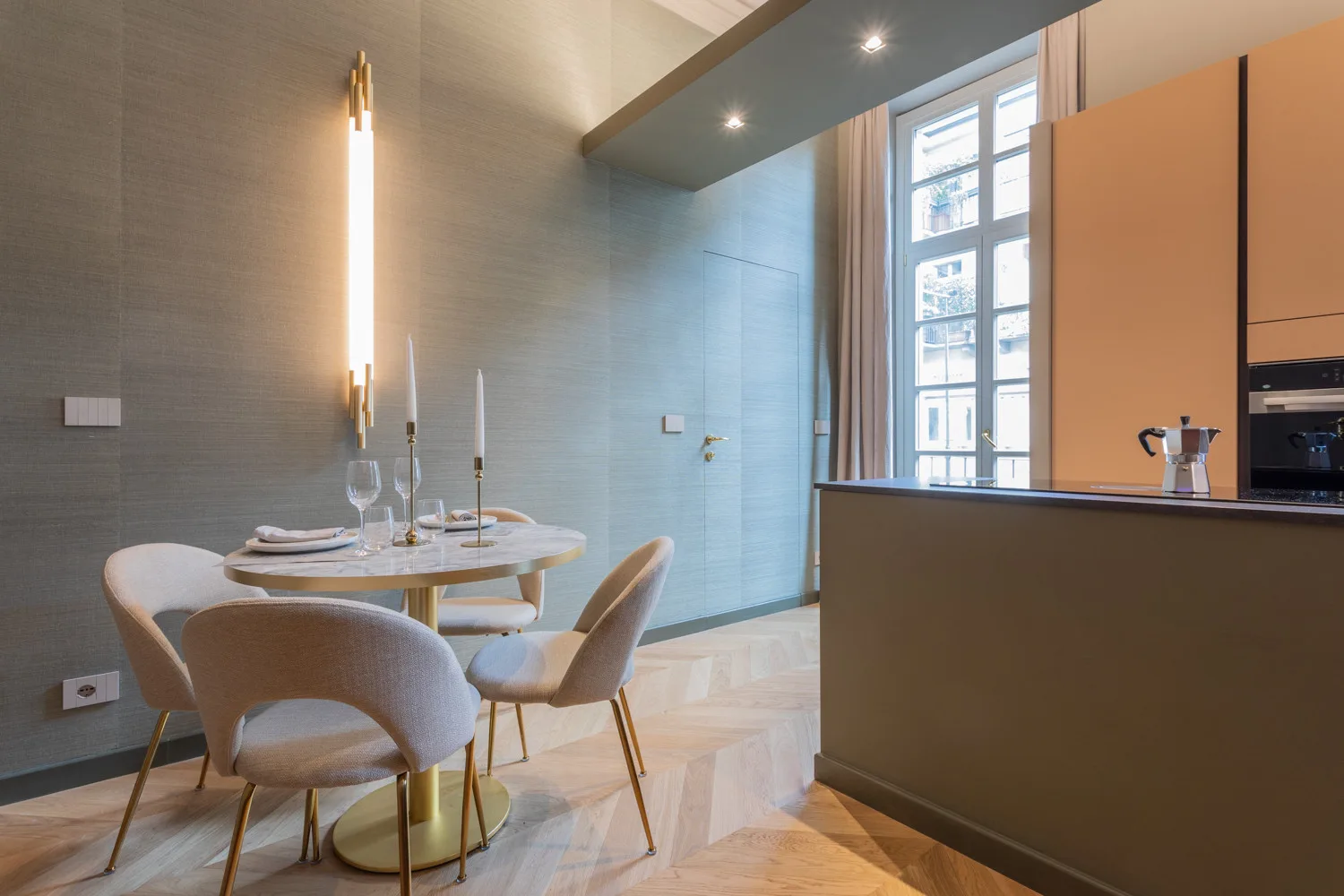 A dining area with a round table and upholstered seating beside a kitchen counter.