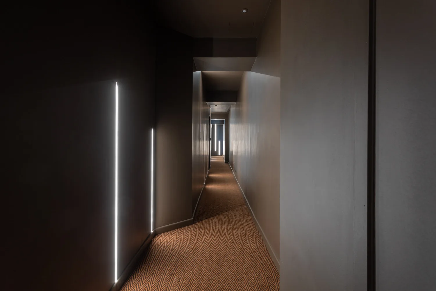 A narrow hallway with dark walls and slim vertical lights.
