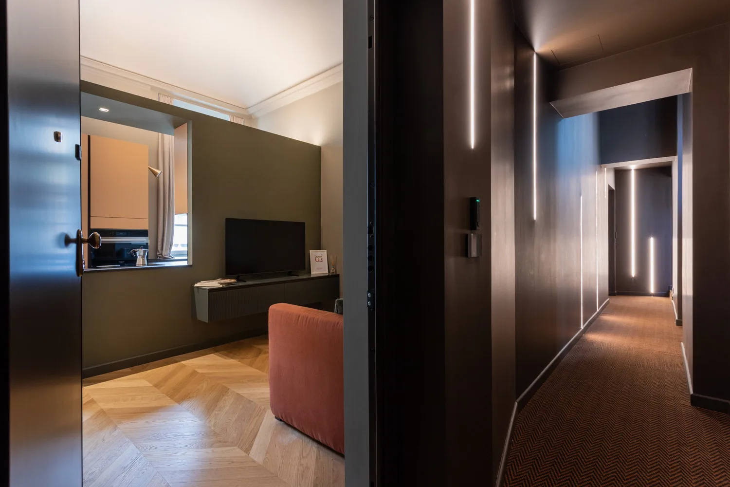 A hotel room opens onto a dim hallway, with a television and seating visible inside.