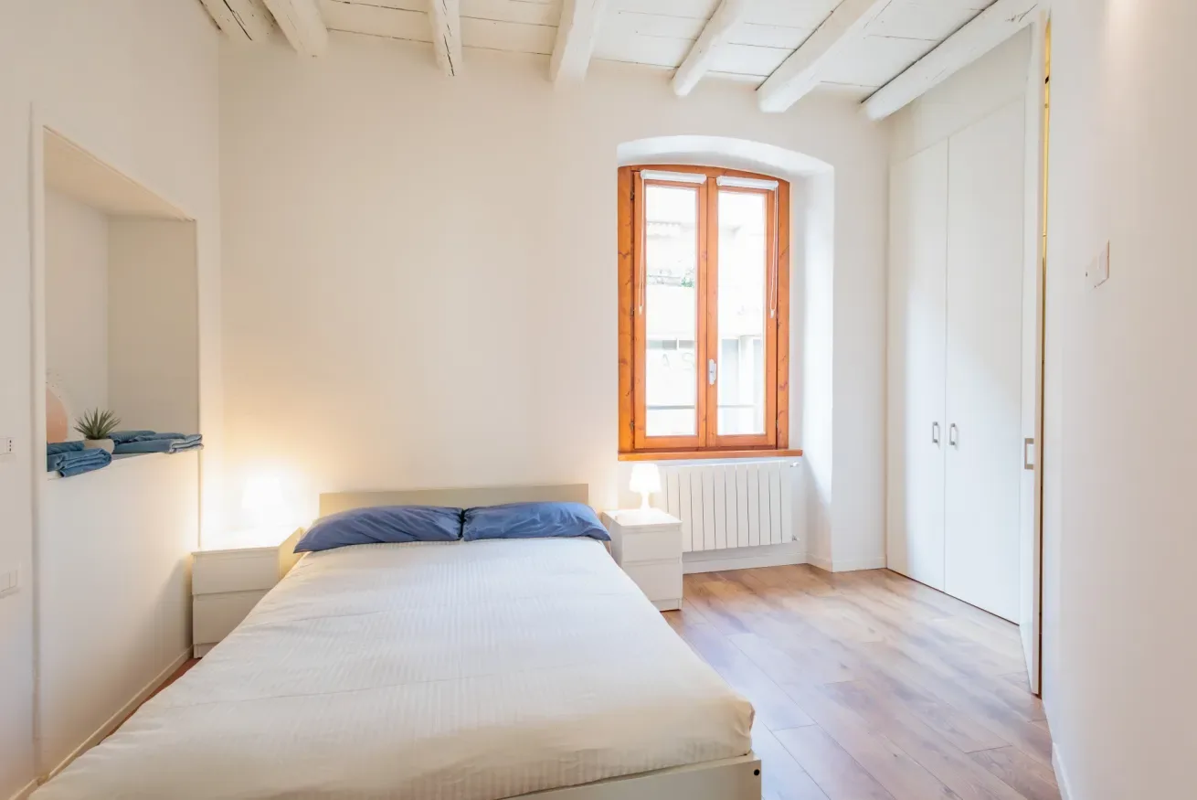 Un dormitorio luminoso con una cama, una ventana con marco de madera y armarios empotrados.