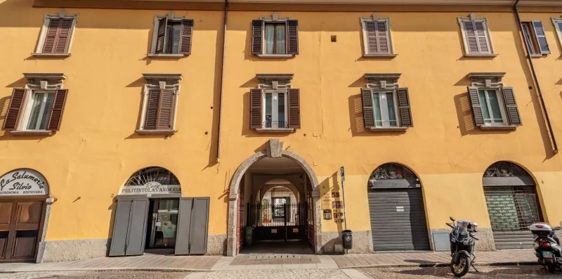 Fachada de un edificio amarillo con ventanas con contraventanas y entradas arqueadas en la planta baja.