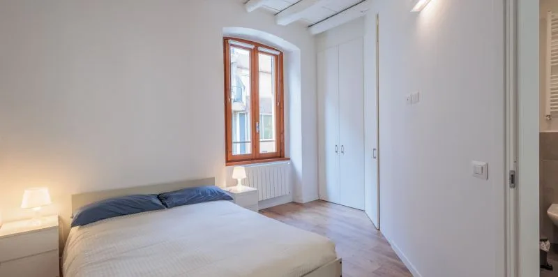 Un dormitorio con una cama bajo una ventana con marco de madera.