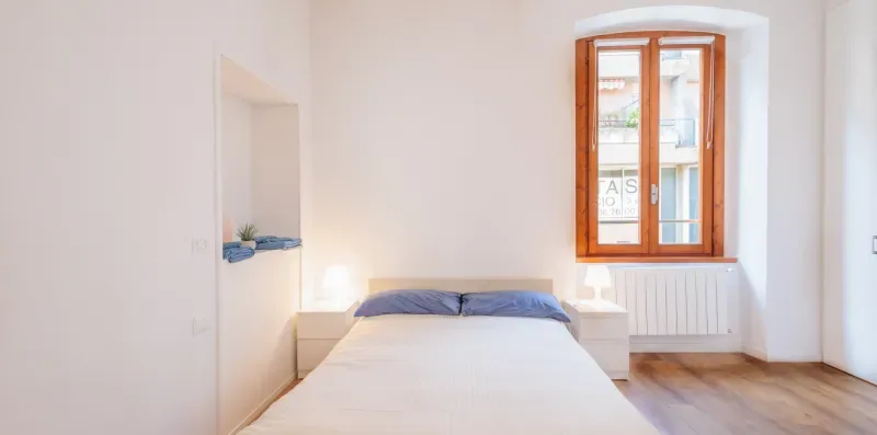 Un dormitorio luminoso con una cama bajo una ventana con marco de madera.