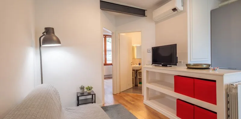 Una sala de estar con asientos, un televisor y una puerta hacia otra habitación.