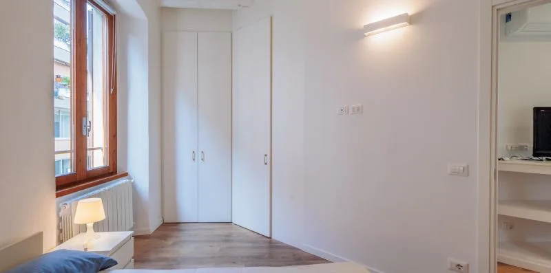Un dormitorio luminoso con una ventana, una cama y armarios empotrados.