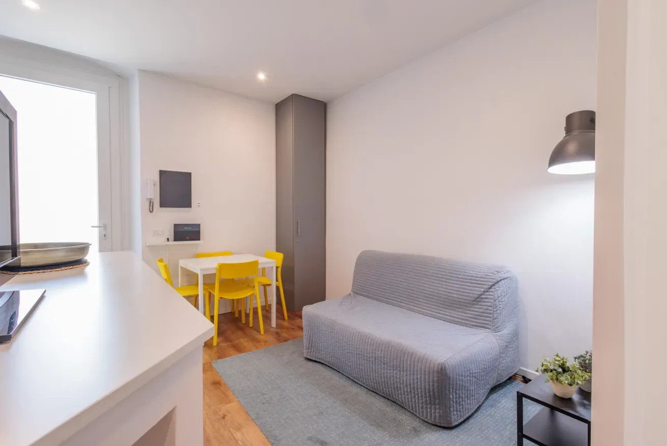 Una pequeña zona de estar y comedor con asientos grises y sillas amarillas.