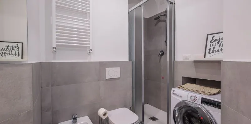 Un baño con ducha, inodoro y lavadora.