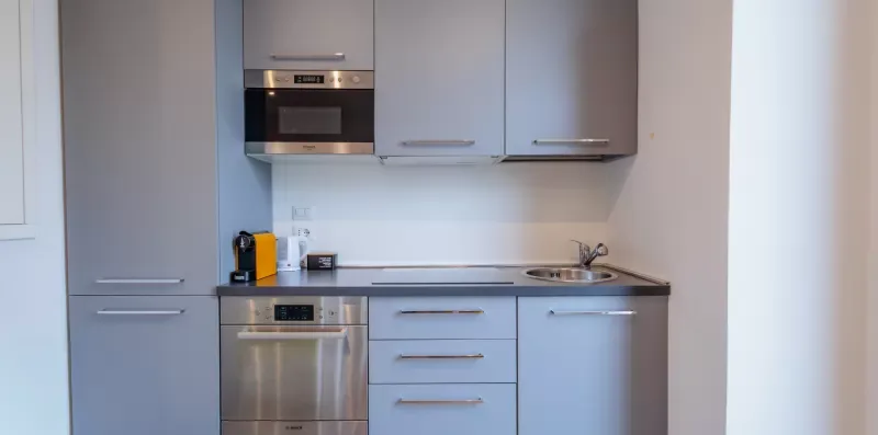 Una cocina compacta con gabinetes claros, un horno empotrado y un fregadero.