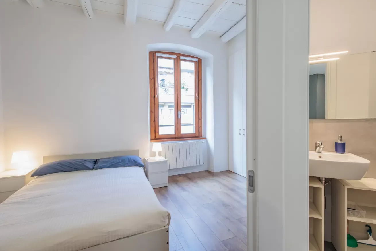 Un dormitorio luminoso con una cama junto a una ventana y una zona de lavabo contigua.