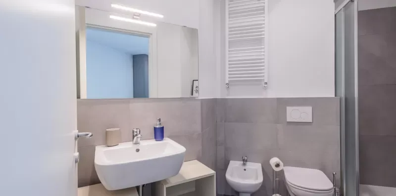 Un baño luminoso con lavabo suspendido y paredes de azulejos grises.
