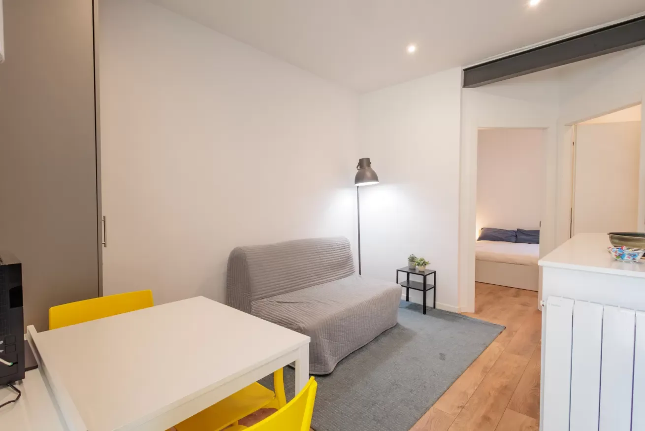 Una pequeña sala de estar con asientos, una mesa y un dormitorio contiguo.