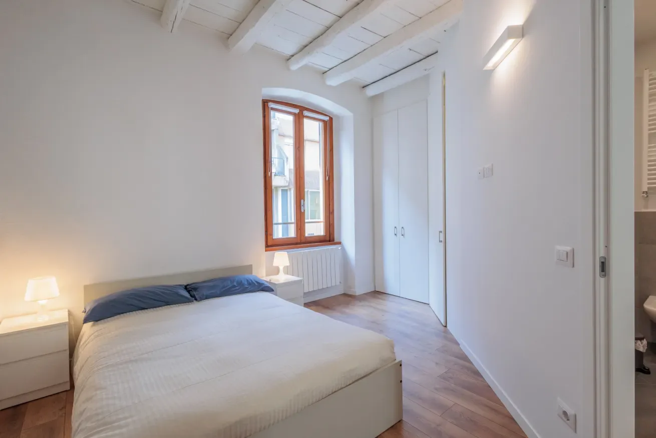 Un dormitorio luminoso con una cama, una ventana con marco de madera y techo inclinado.