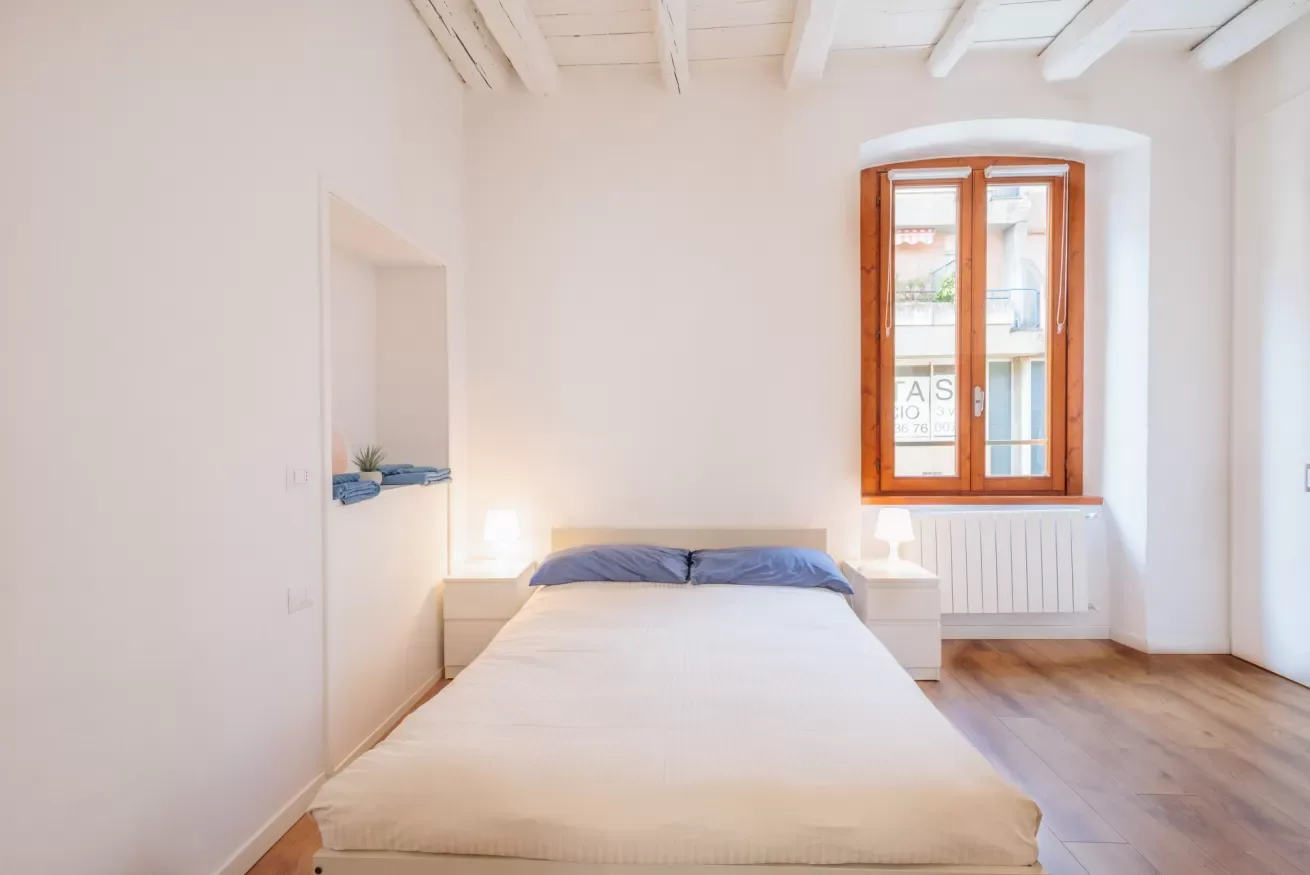 Un dormitorio luminoso con una cama bajo una ventana con marco de madera.