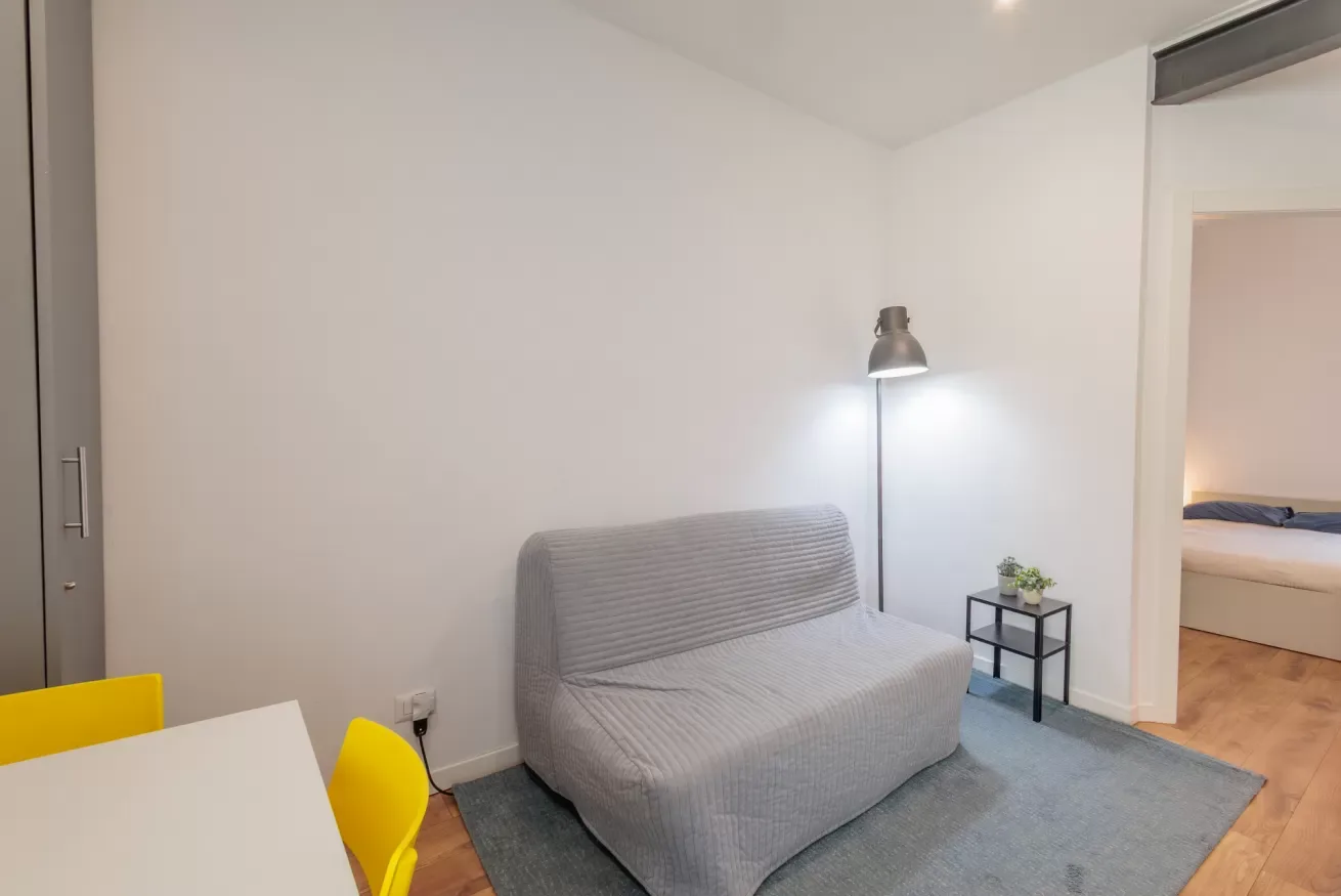 Una zona de estar con un sofá gris, una lámpara de pie y una mesita auxiliar.