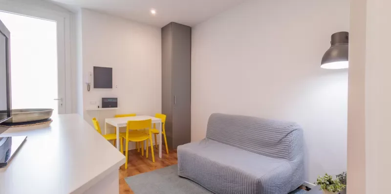 Una pequeña sala de estar con un sofá gris, sillas amarillas y una barra blanca.