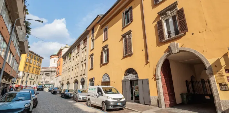 Una calle urbana estrecha bordeada de edificios de varias plantas y coches aparcados.