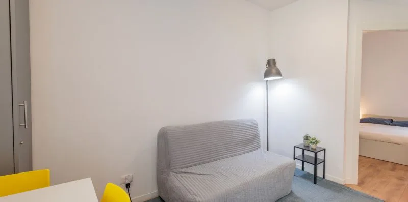 Una sala de estar con asiento gris, una lámpara de pie y una mesita auxiliar.