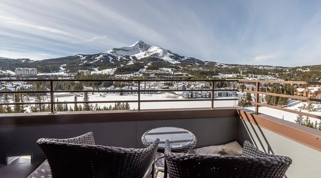 Un balcón da a un paisaje montañoso nevado, con asientos oscuros junto a la barandilla.
