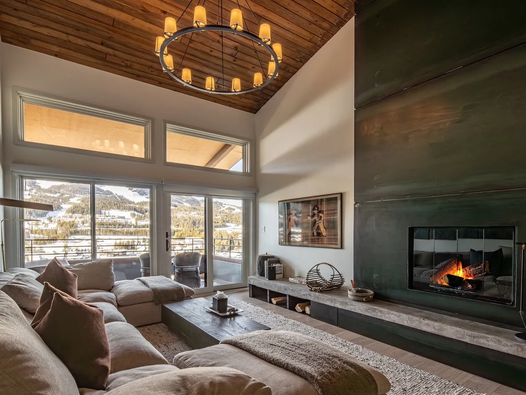 Una sala de estar con asientos, una chimenea y vistas a montañas nevadas por las ventanas.