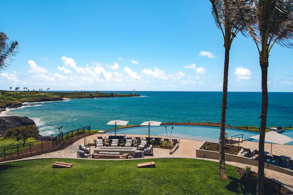 Un patio junto al mar da a aguas turquesas, con asientos al aire libre bajo sombrillas.