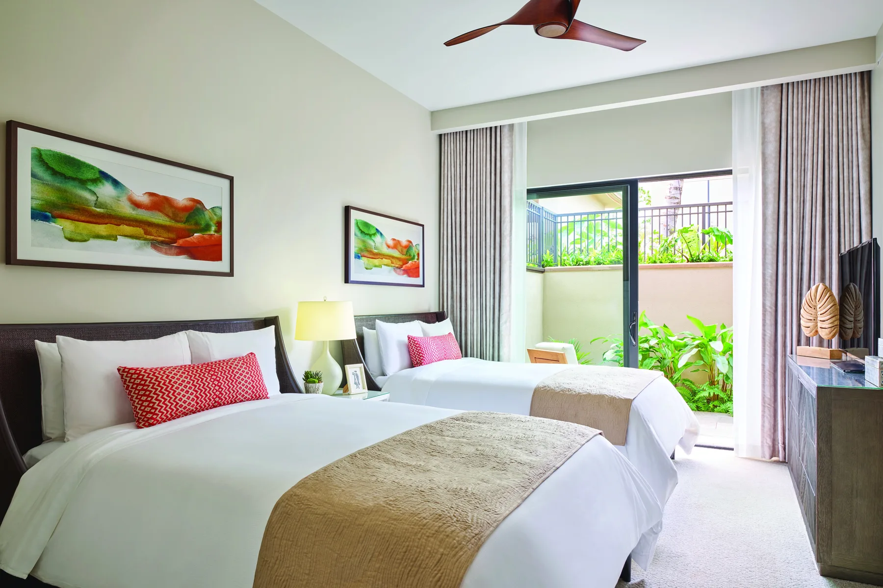 Un dormitorio luminoso con dos camas, cuadros coloridos y vistas al jardín.