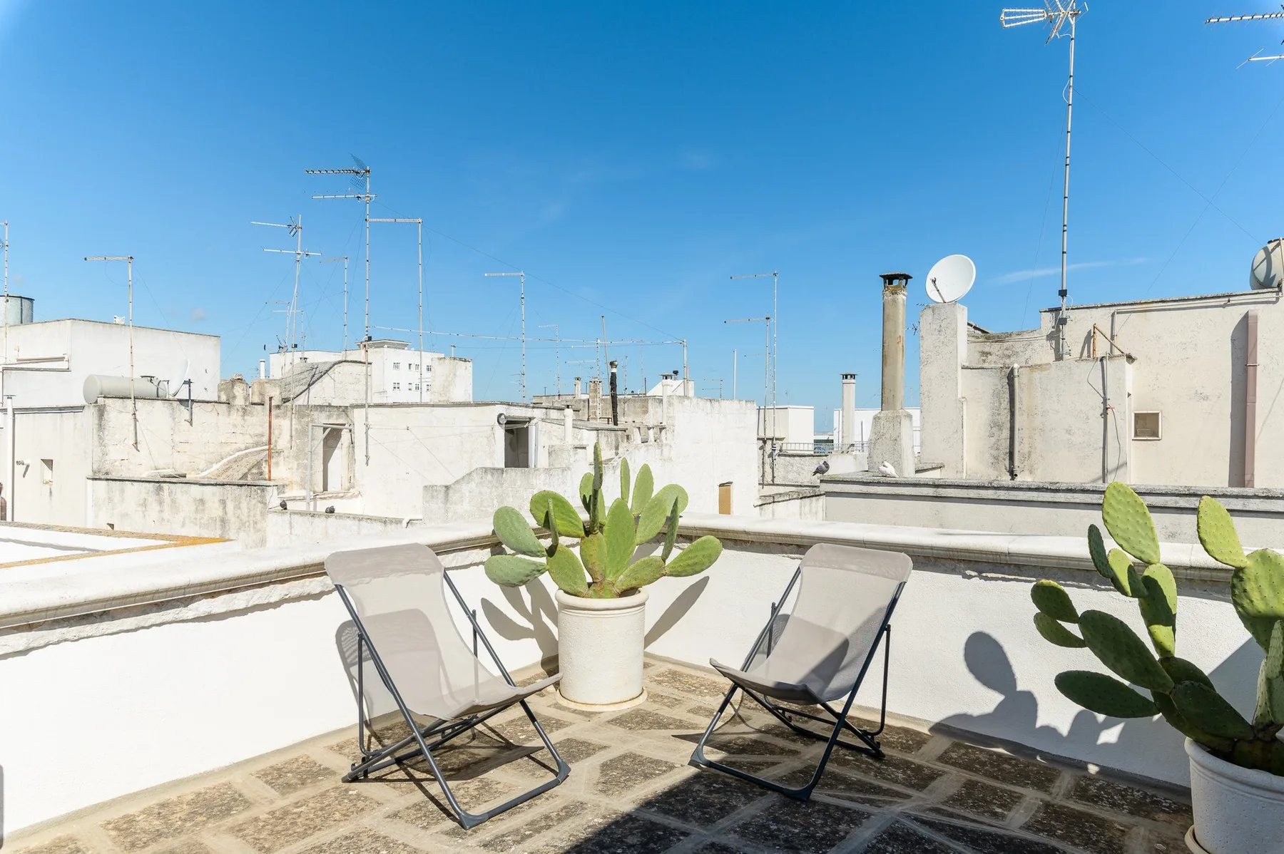 A rooftop terrace with folding seating and potted plants overlooks nearby buildings.