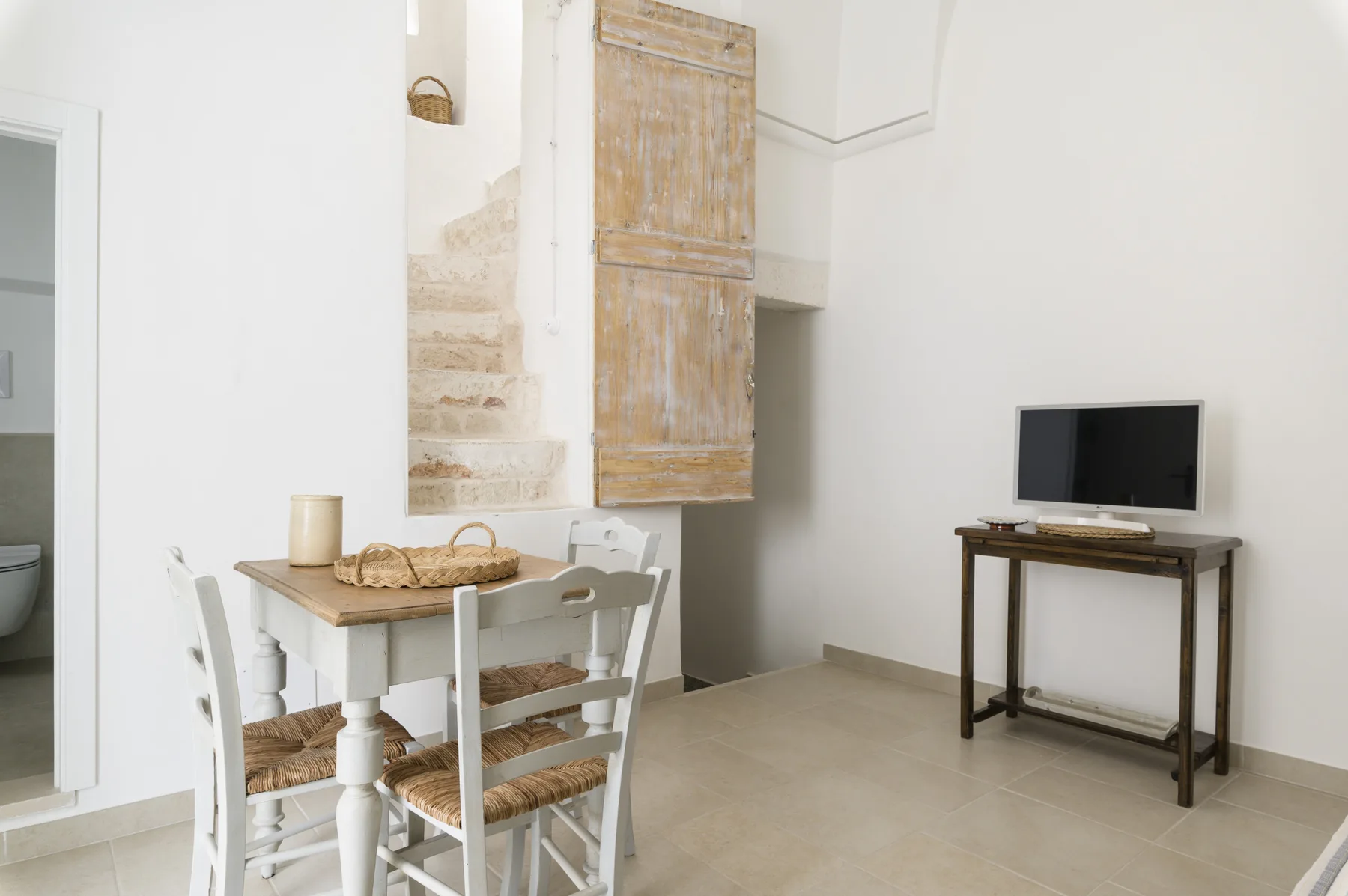 A bright dining area with a small table beside a staircase and television.