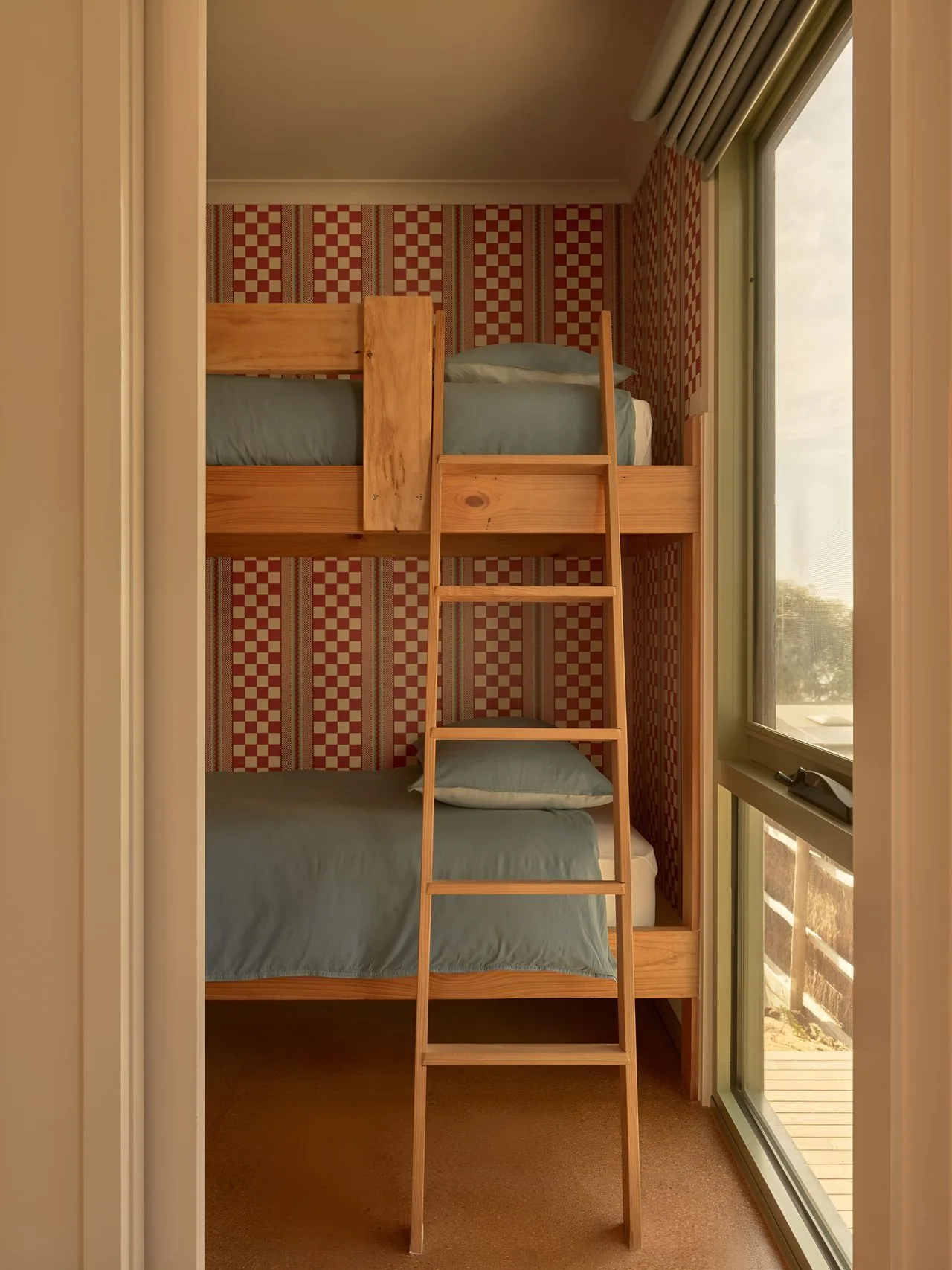 A compact bedroom with wooden bunk beds and a ladder beside a large window.