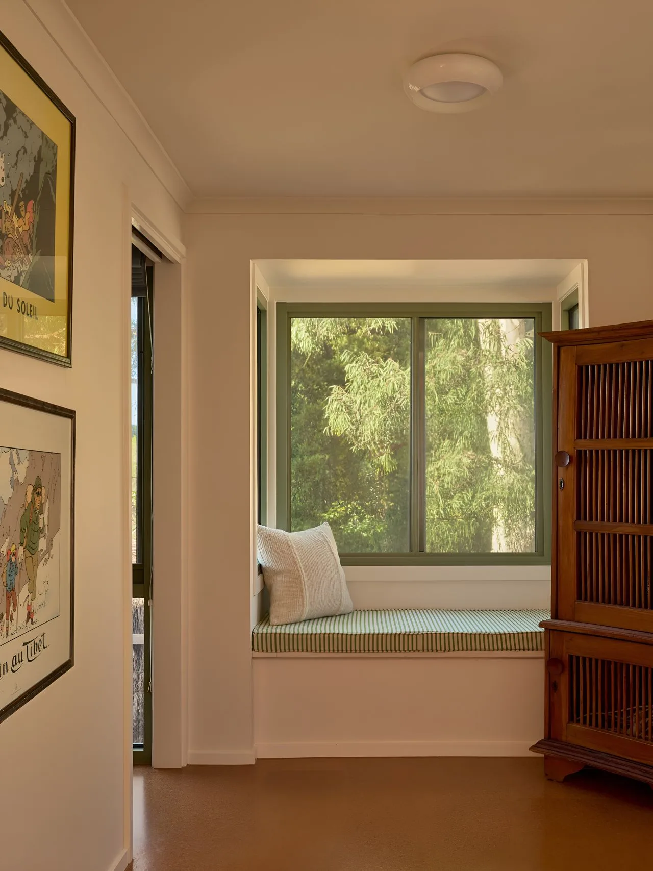 A bright room with a window seat overlooking leafy trees.